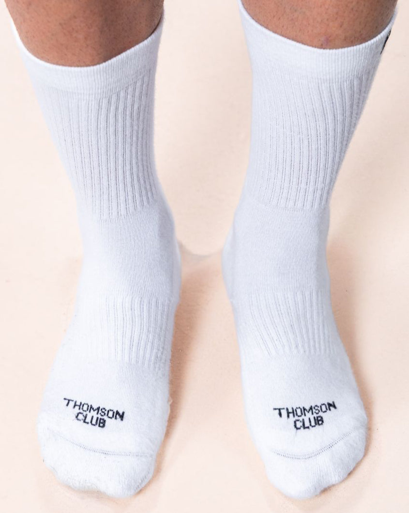 Meias TC brancas em algodão macio (80% algodão, 15% poliamida, 5% elastano). Design sem costura para máximo conforto. Altura de 12 cm do calcanhar ao topo, logotipo Thomson Club em jacquard e etiqueta TC preta. Perfeitas para uso diário.