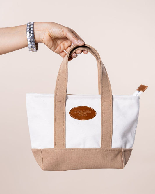 Mini bolsa TC cru-taupe, feita em lona pesada de 500 gr, com interior forrado e alças reforçadas para transporte à mão. Patch de couro premium com logotipo Thomson Club em relevo positivo, fecho de correr com puxador TC personalizado em couro premium. Tamanho compacto (22x10x19 cm), perfeita para completar qualquer look com um toque de sofisticação.