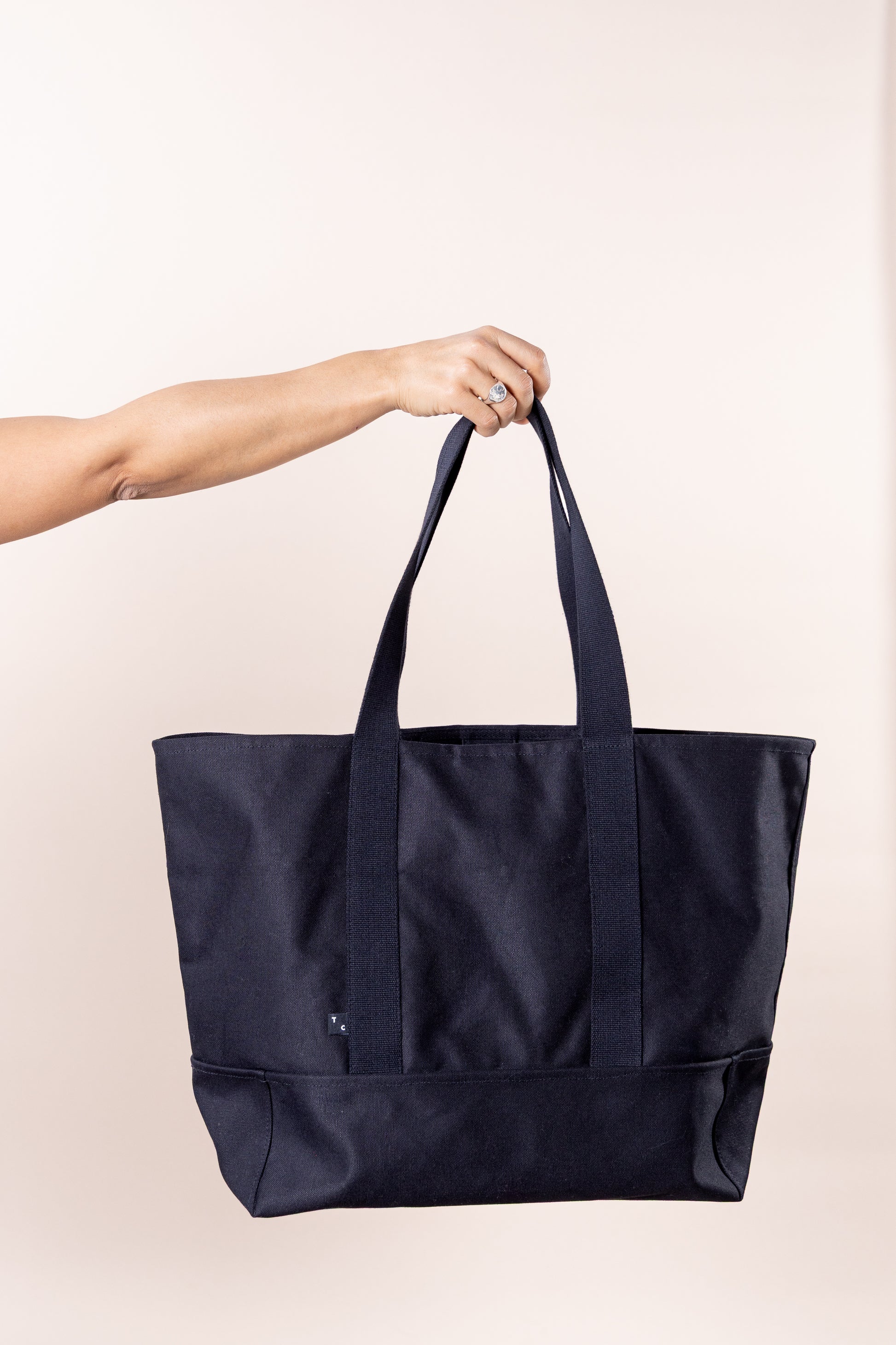 Saco estruturado e espaçoso, ideal para o dia a dia. Feito em lona pesada 500g/m², 100% algodão preto, combina resistência e estilo. Com alças reforçadas para uso na mão ou ombro, mede 38x18x36 cm. Possui bolso interno com tag metálica prateada, logotipo Thomson Club bordado, etiqueta bandeira TC e botão de pressão. Qualidade e design atemporal.
