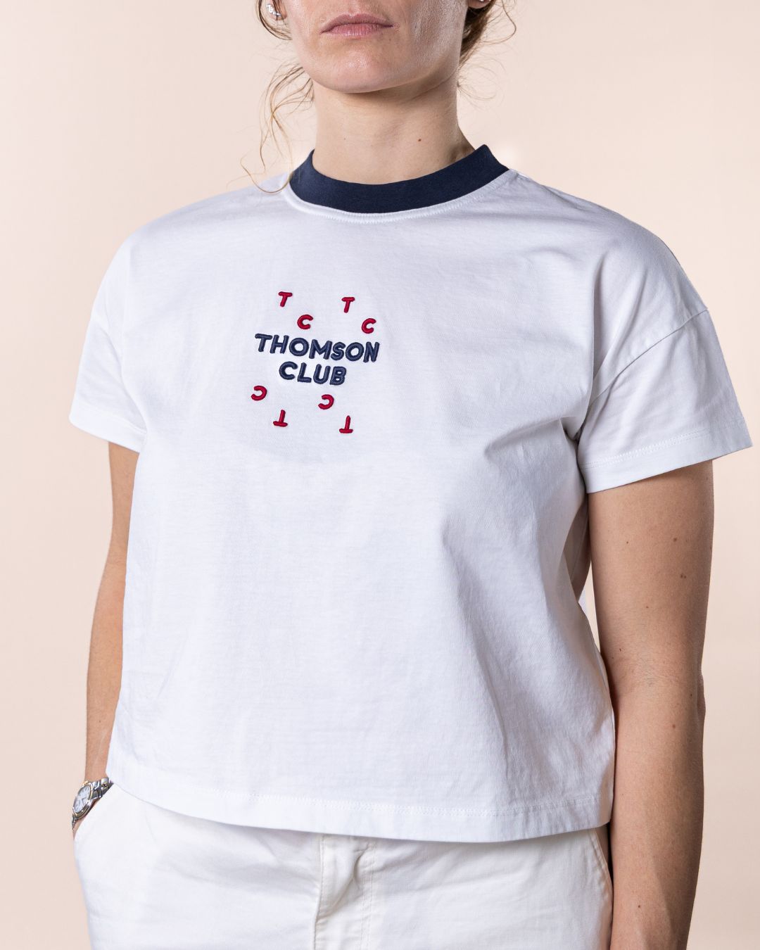 T-shirt feminina branca confecionada em 100% algodão orgânico, jersey de 200g, com corte ligeiramente curto mas relaxado. Apresenta gola em rib 1x1, costuras detalhadas de alta qualidade, meia-lua nas costas para maior conforto, bordado em relevo Thomson Club e tag metálica em prata velha. Produção sustentável e design sofisticado, ideal para diversas ocasiões.
