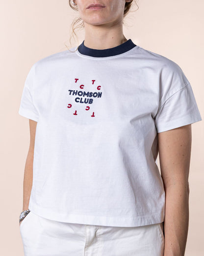 T-shirt feminina branca confecionada em 100% algodão orgânico, jersey de 200g, com corte ligeiramente curto mas relaxado. Apresenta gola em rib 1x1, costuras detalhadas de alta qualidade, meia-lua nas costas para maior conforto, bordado em relevo Thomson Club e tag metálica em prata velha. Produção sustentável e design sofisticado, ideal para diversas ocasiões.