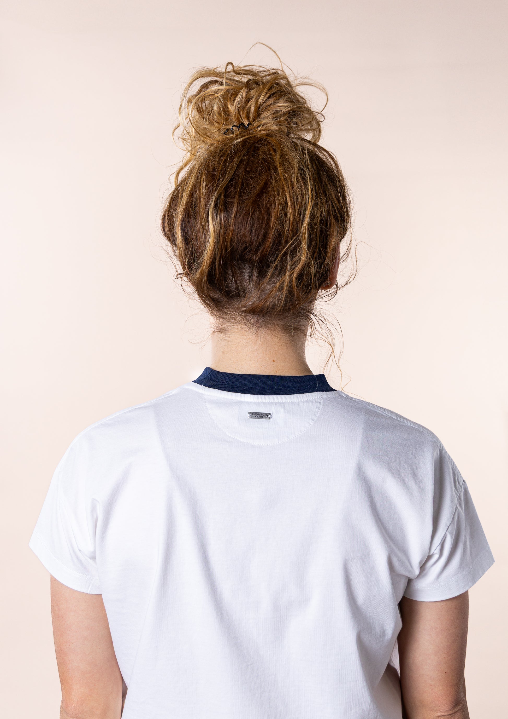 T-shirt feminina branca confecionada em 100% algodão orgânico, jersey de 200g, com corte ligeiramente curto mas relaxado. Apresenta gola em rib 1x1, costuras detalhadas de alta qualidade, meia-lua nas costas para maior conforto, bordado em relevo Thomson Club e tag metálica em prata velha. Produção sustentável e design sofisticado, ideal para diversas ocasiões.