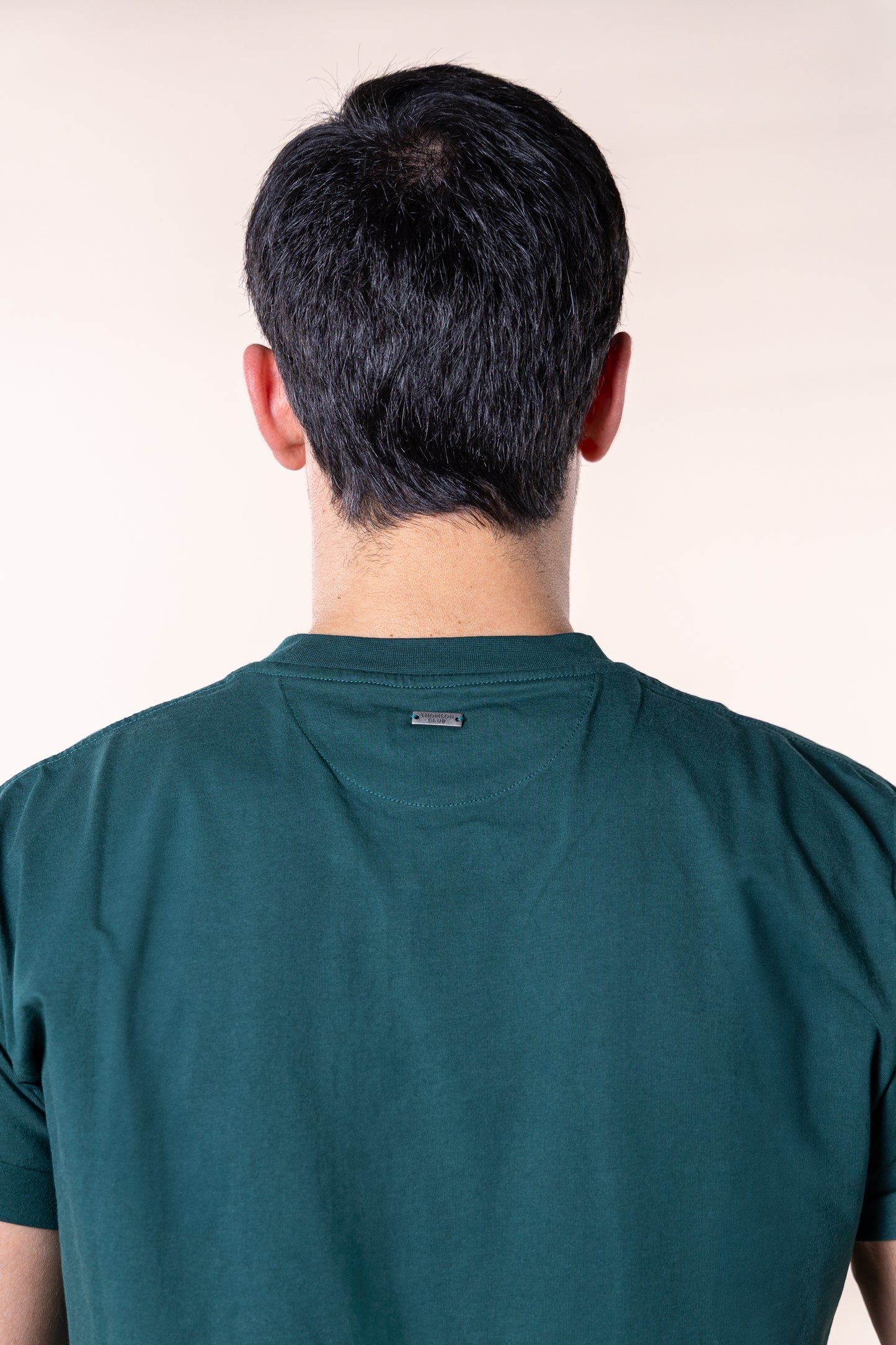 T-shirt verde de homem em algodão orgânico, corte relaxado com gola rib 1X1 e costuras de alta qualidade. Logotipo Thomson Club bordado em relevo e tag metálica nas costas. Visual simples e versátil, ideal para diversas combinações e ocasiões do dia a dia, equilibrando estilo clássico e desportivo.